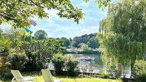 A garden with a lawn, two white lounge chairs, a small pond, and a boat on the water. - Lux 8Br Thamesfront Villa w/ Yacht & Sauna (Staines)