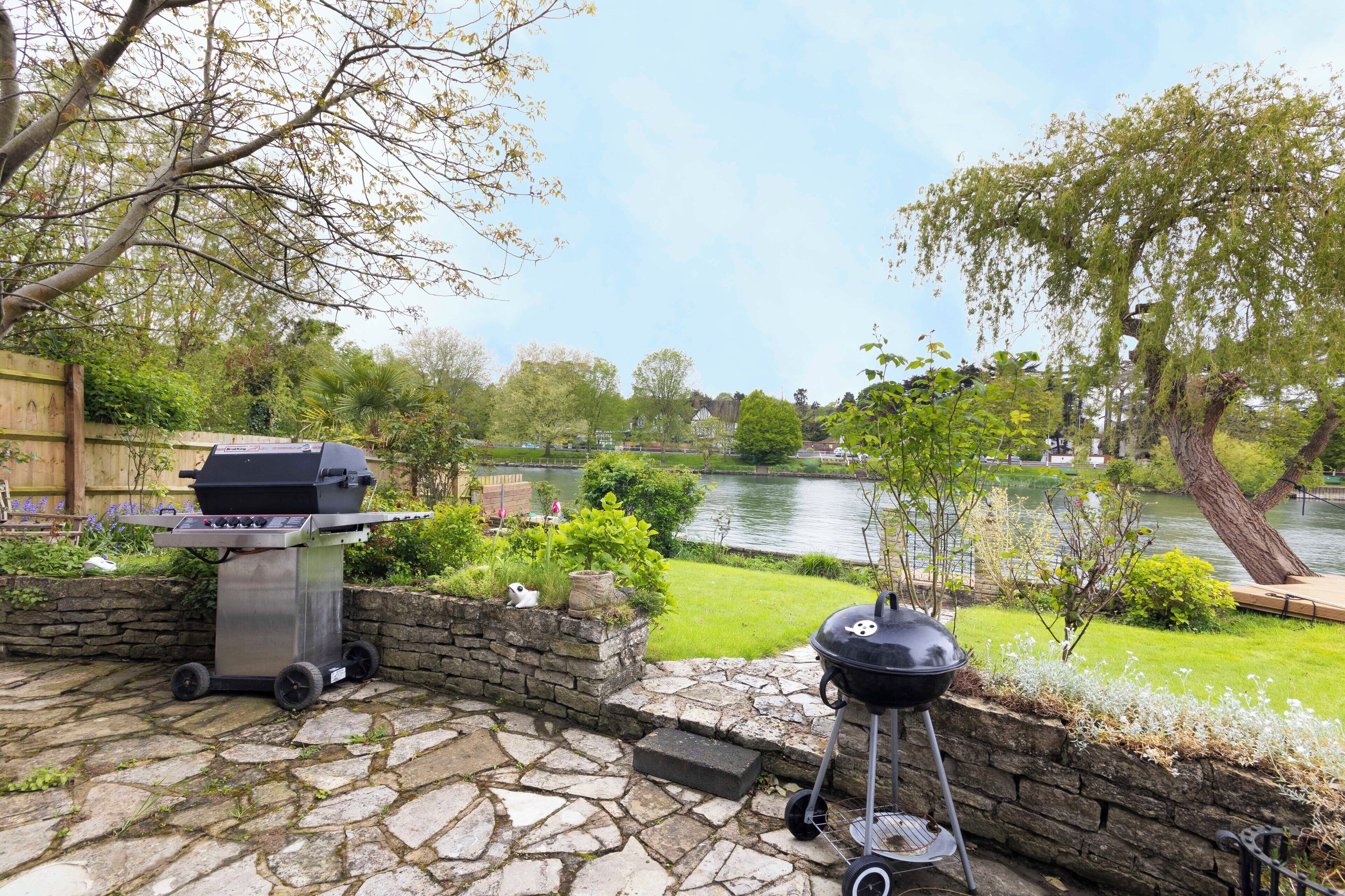 Un patio al aire libre con suelo de piedra, una parrilla portátil y vistas a un lago.
