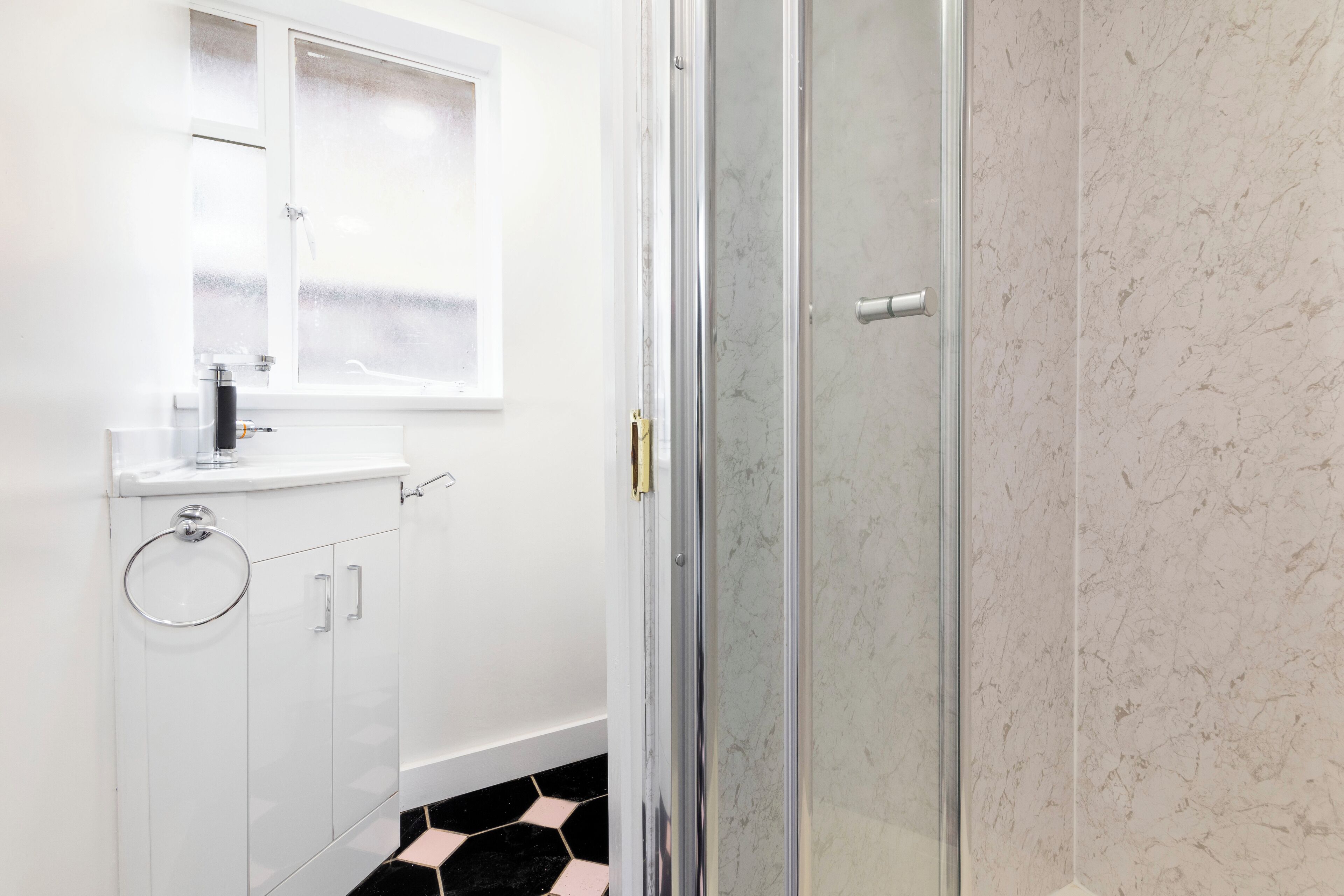 A bathroom with a glass shower enclosure, a white sink with a mirror, and a tiled floor.