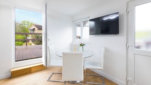 A modern dining area with a glass table, white chairs, and a TV mounted on the wall. - Lux 8Br Thamesfront Villa w/ Yacht & Sauna (Staines)