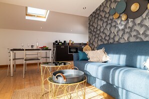 En moderne stue med en blå sofa, et spisebord med stole og et køkken i baggrunden.