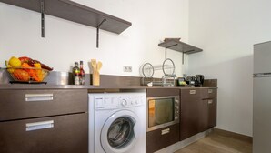 Moderni keittiö, jossa on sisäänrakennettu pesukone ja kuivausrumpu, puiset kaapit ja hedelmäkulho työtasolla.