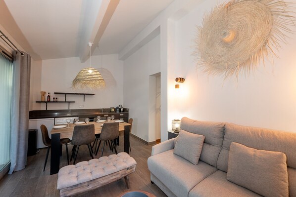 Un salon moderne avec un canapé, une table à manger dressée pour quatre personnes et un coin cuisine en arrière-plan.