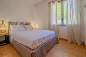 A bedroom with a bed, bedside lamps, a window with curtains, and a wooden floor.