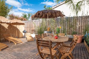 Une terrasse extérieure avec des meubles en bois, un barbecue et un parasol en chaume.