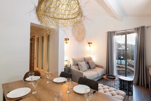 A modern dining area with a wooden table set for six, a sofa, and a balcony with a grill. - Private Garden La Cabane Bambou Mandara Beach (Juan-les-Pins)