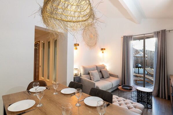 A modern dining area with a wooden table set for six, a sofa, and a balcony with a grill.