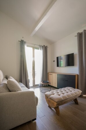 A modern living room with a sofa, a wooden ottoman, a TV, and a sliding glass door to the outside.