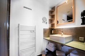 Ein modernes Badezimmer mit einem weißen Heizkörper, einem Waschbecken mit Spiegel darüber und Holzregalen.