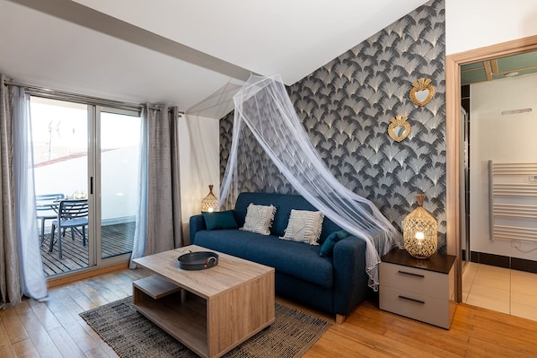 Ein modernes Wohnzimmer mit einem blauen Sofa, einem Holztisch und einer Glastür, die zu einem Außenbereich führt.