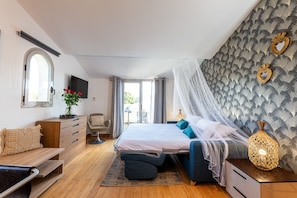 Ein Schlafzimmer mit Bett, Kommode, Sessel, Fernseher und Blick ins Freie.