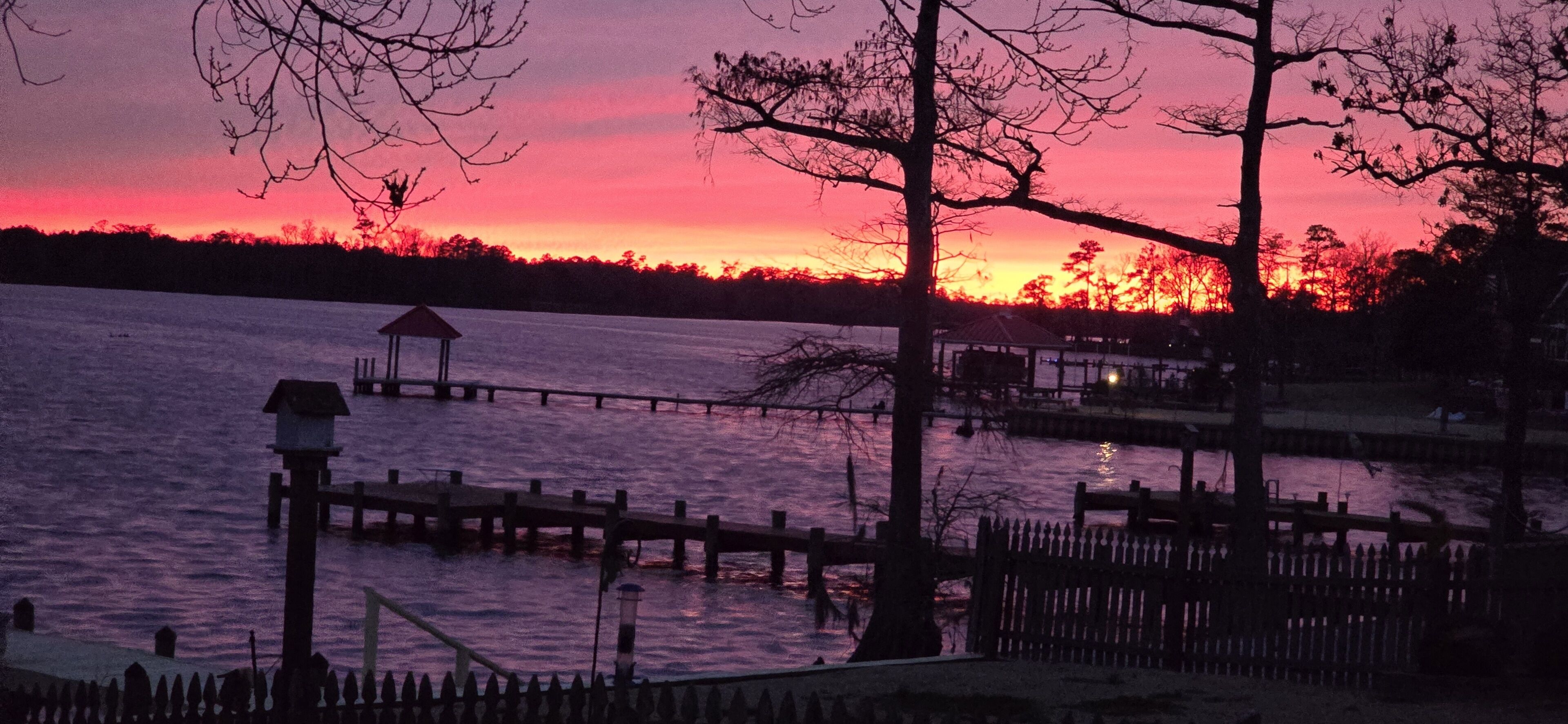 A waterfront scene with a dock extending into a body of water, surrounded by trees and a gazebo-like structure.