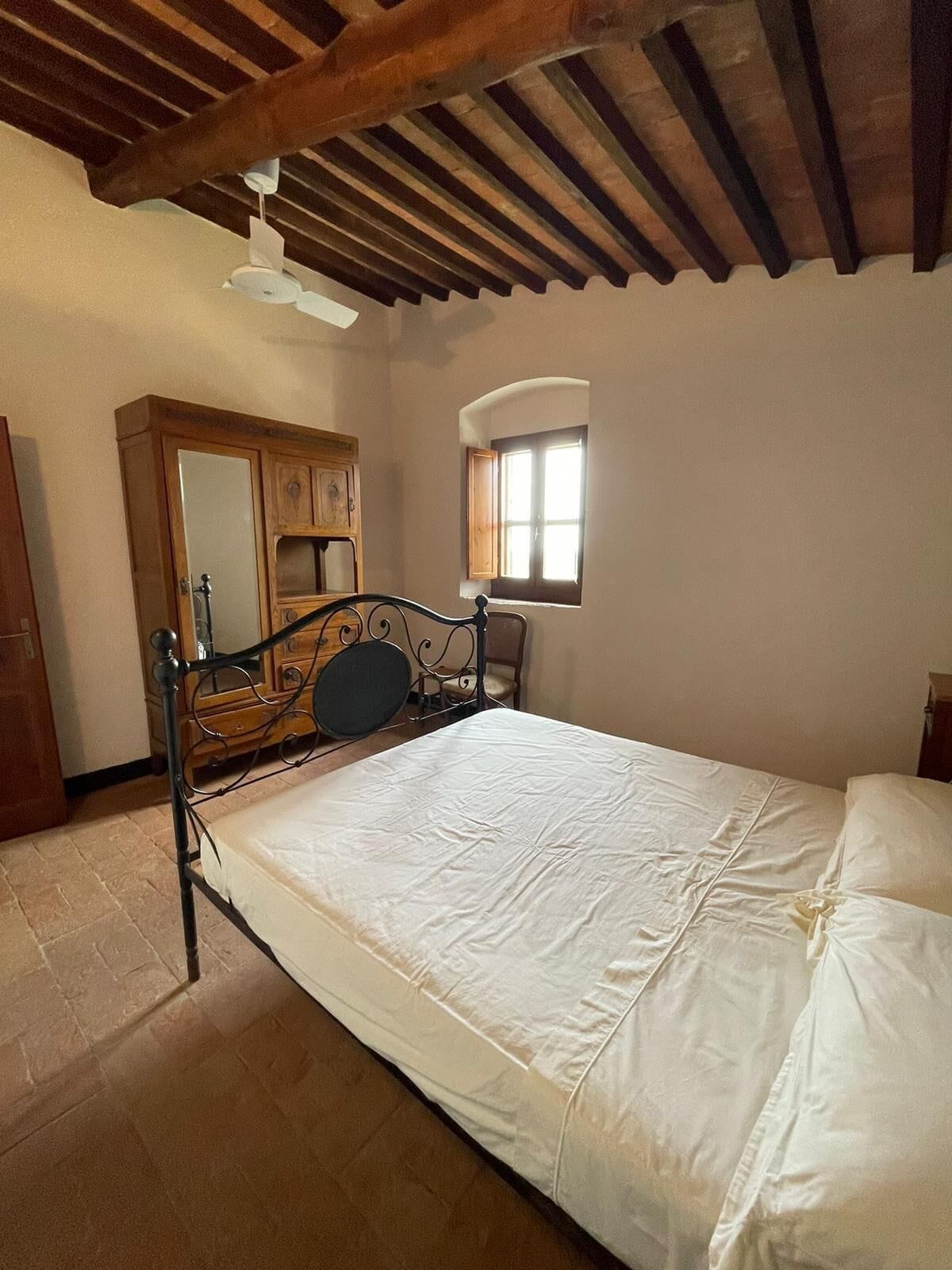 A bedroom with a bed, wooden headboard, a small window, and a ceiling fan.
