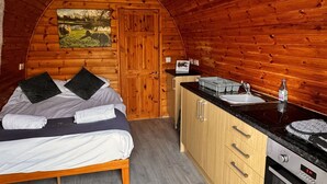 Ein gemütlicher Holzraum mit Bett, Gemälde, Küchenzeile und Holztür.