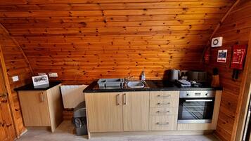 A compact kitchen with wooden walls, a sink, a stove, and cabinets.