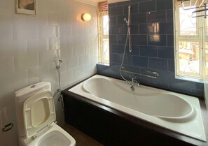 A bathroom with a white toilet, a bathtub, and a window with a view. - Family-sized unique private villa w/an office & kitchen, super close to the city (Kampala)