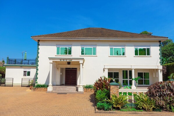 A two-story building with a tiled roof, a central entrance with a wooden door, and a sign above the door. - Family-sized unique private villa w/an office & kitchen, super close to the city (Kampala)