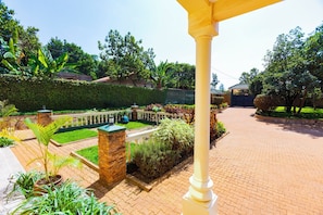 A well-maintained garden with a paved walkway, a stone wall, and various plants. - Family-sized unique private villa w/an office & kitchen, super close to the city (Kampala)
