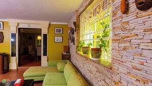 A room with a green sofa, a stone wall, and potted plants.