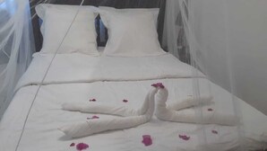 A bed with white linens, a canopy, and decorative swan-shaped pillows.