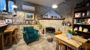 Una habitación acogedora con chimenea de piedra, un sillón verde azulado, muebles de madera y una estantería.