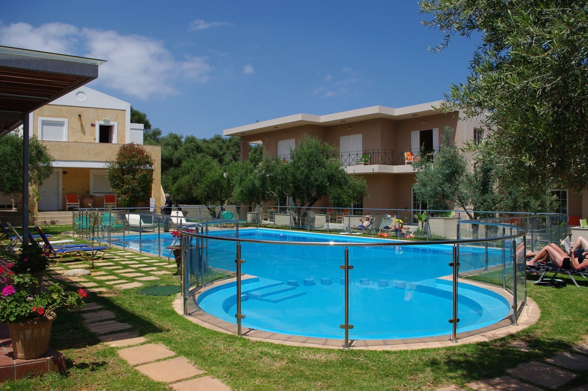 A swimming pool with a surrounding deck, a covered seating area, and a building with balconies in the background.