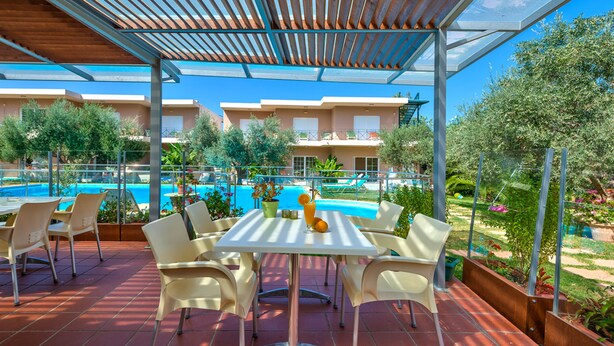 A covered outdoor seating area with a pool view, white chairs, and a table with a drink. - Cozy Studio with Swimming Pool Near the Sea (Chania)