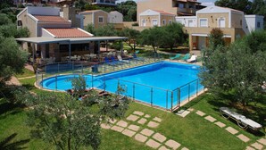 A swimming pool surrounded by a deck with lounge chairs, a covered seating area, and a view of residential buildings.