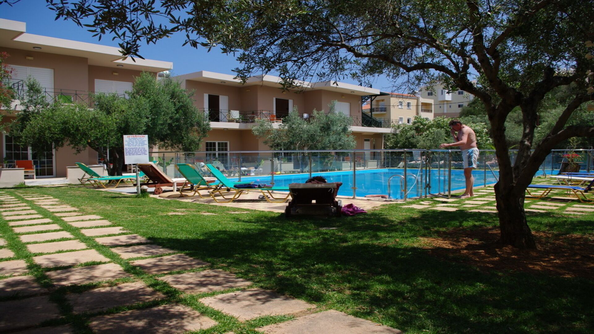 Area piscina con lettini, piscina e un albero.