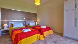 A hotel room with two beds, each with colorful bedding, a wooden headboard, a nightstand with a lamp, and a wardrobe. - Cozy Apartment with Swimming Pool Near the Sea (Chania)