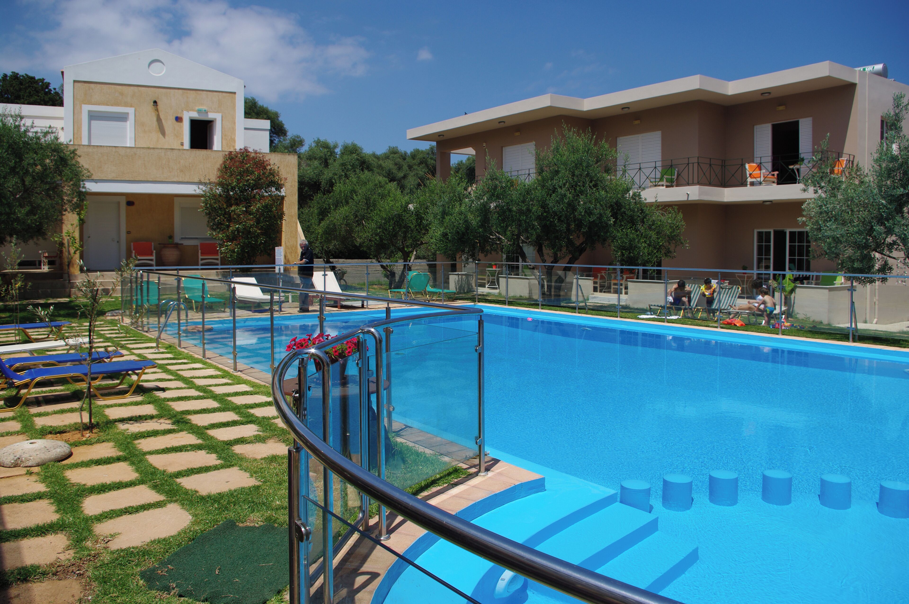 A swimming pool with a glass barrier, sun loungers, and a building with balconies.