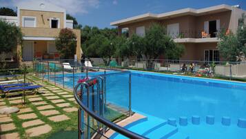 A swimming pool with a glass barrier, sun loungers, and a building with balconies.