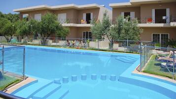 Une piscine avec un bassin aux eaux d’un bleu limpide, entourée d’une petite clôture. On y trouve des chaises longues et un petit espace aménagé avec vue sur un immeuble à plusieurs étages doté de balcons.