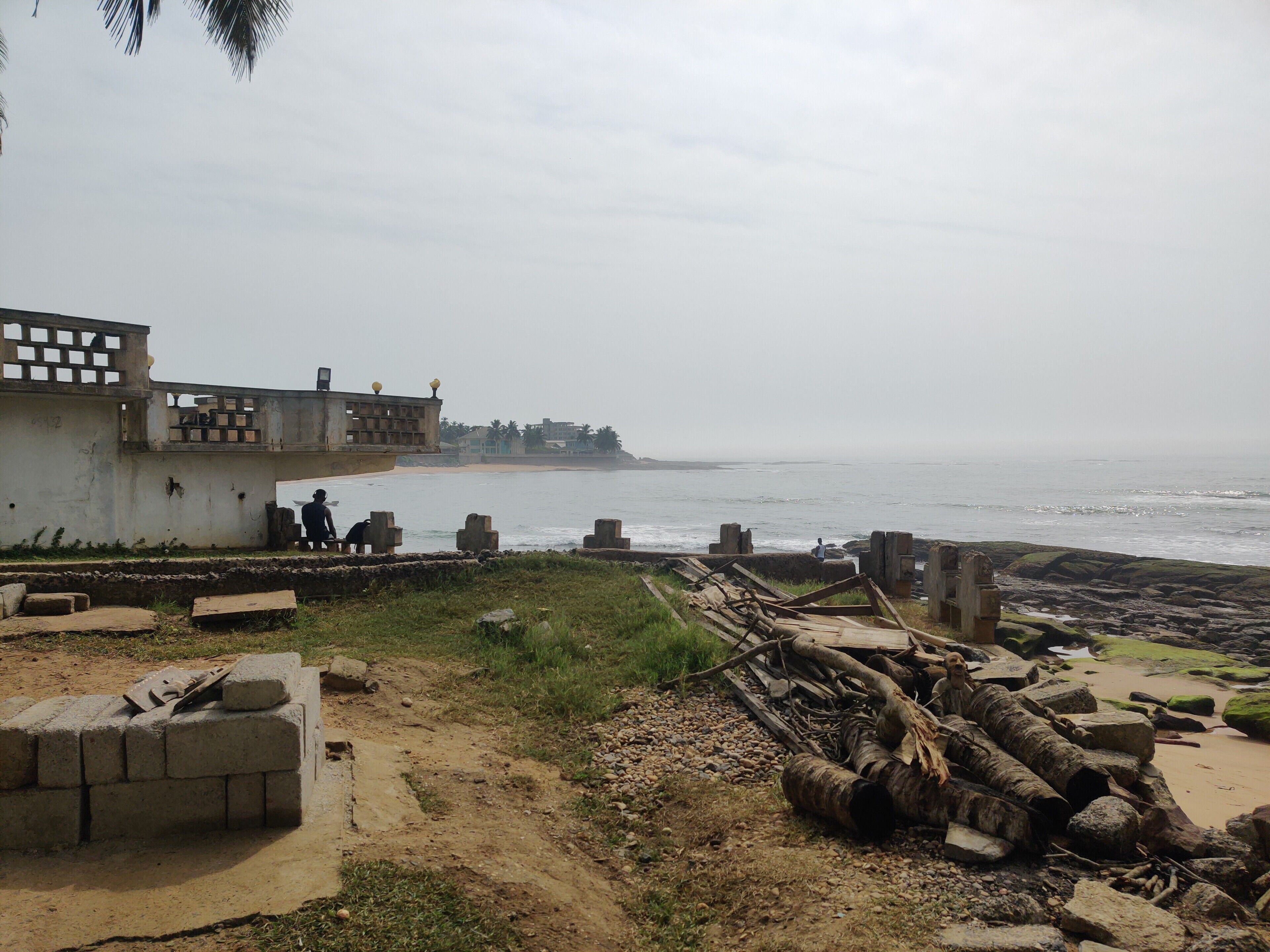 A coastal view with a concrete structure, a sandy beach, and scattered debris.