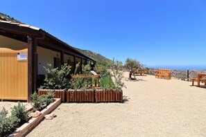 A building with a covered patio area, wooden benches, and a view of the ocean. - Agriturismo Dispenza (Collesano)