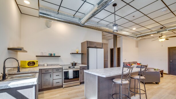 A modern kitchen with a central island, bar stools, and a dining area with a sofa and table.