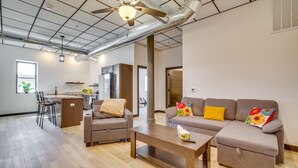 A modern living room with a sofa, chairs, a coffee table, and a kitchen area in the background.