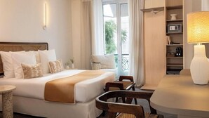 A hotel room with a bed, bedside table, chairs, a desk, a lamp, a shelf with items, and a window with curtains. - Sonder Yelo Lumiere (Cannes)