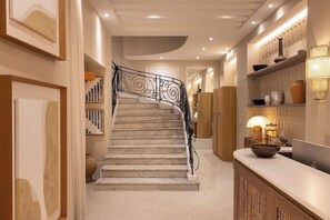 A staircase with a black railing, a marble floor, and a wall with shelves and decorative items.