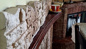 Pared de piedra con un repisa de madera, chimenea de ladrillo y suelo de baldosas.