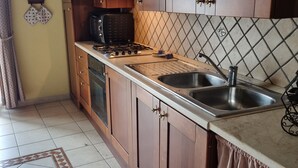Una cocina con armarios de madera, estufa a gas, lavamanos y salpicadero de azulejos.