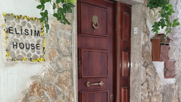 Un edificio de piedra con puerta de madera, un letrero que dice "ELISIM HOUSE" y una ventana pequeña.