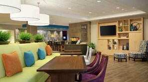 Un lobby moderno de hotel con una zona de estar, un bar y un televisor.