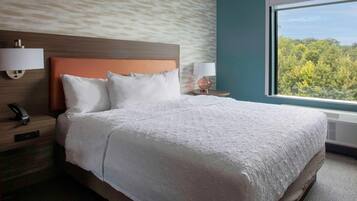 Habitación de hotel con una cama grande, dos mesitas de noche con lámparas, un teléfono en la pared y una ventana con vistas a árboles.