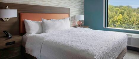 A hotel room with a large bed, two bedside tables with lamps, a wall-mounted phone, and a window with a view of trees.