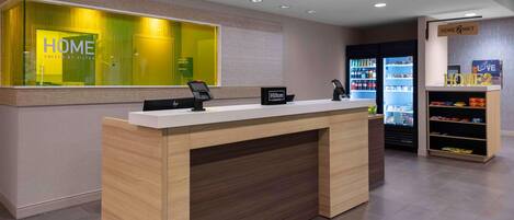 A modern hotel reception desk with a digital kiosk, a minibar, and a vending machine.