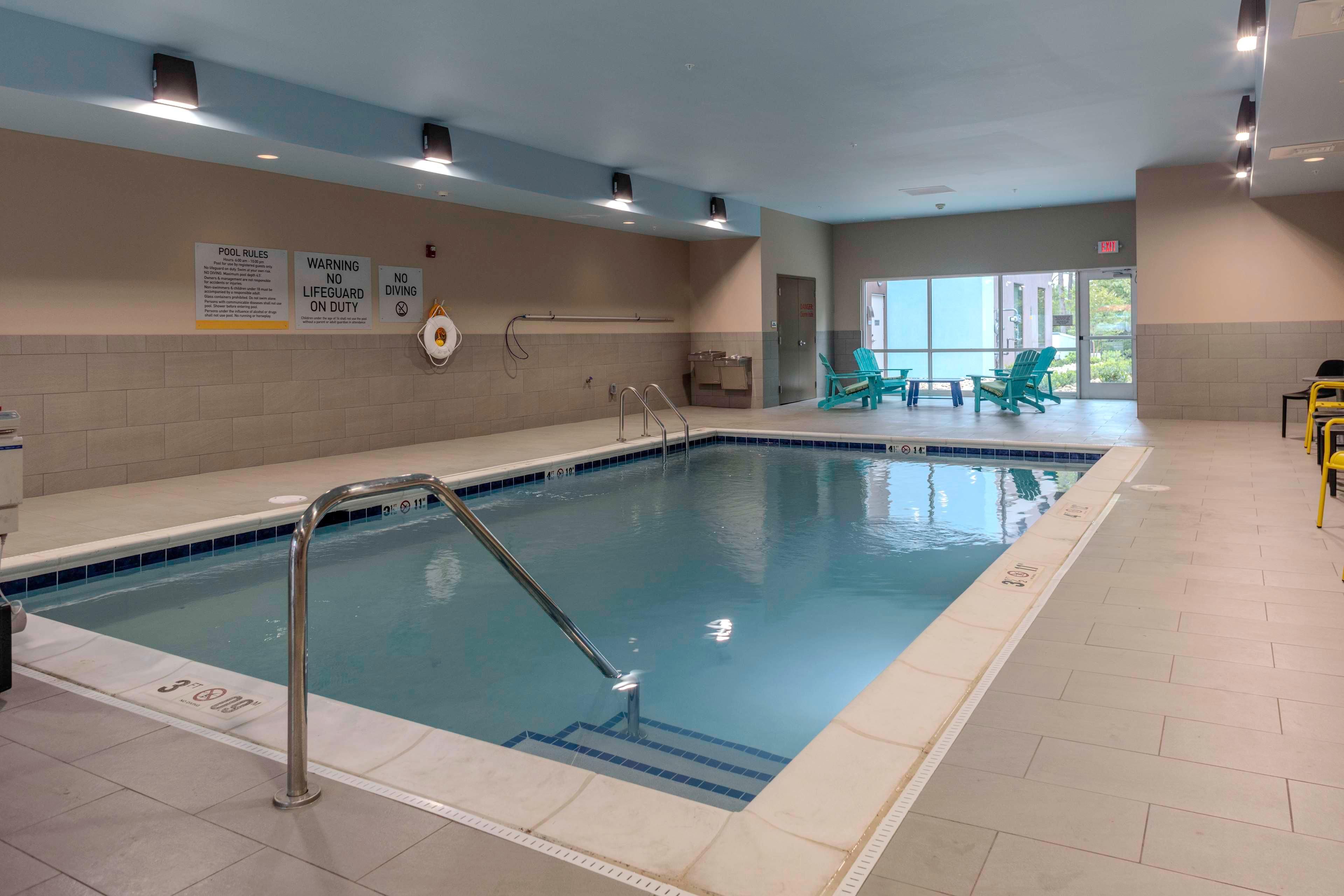 Una piscina techada con normas claras para bañistas y avisos de seguridad en las paredes, un asiento de salvavidas y un puesto de socorrista.
