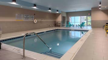 An indoor swimming pool with clear pool rules and safety warnings on the walls, a lifeguard chair, and a lifeguard stand.