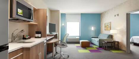 Une chambre d’hôtel moderne équipée d’une kitchenette, d’un canapé, d’un bureau et d’une télévision.