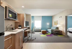 Una habitación de hotel compacta con kitchenette, un sofá, un escritorio y un televisor.